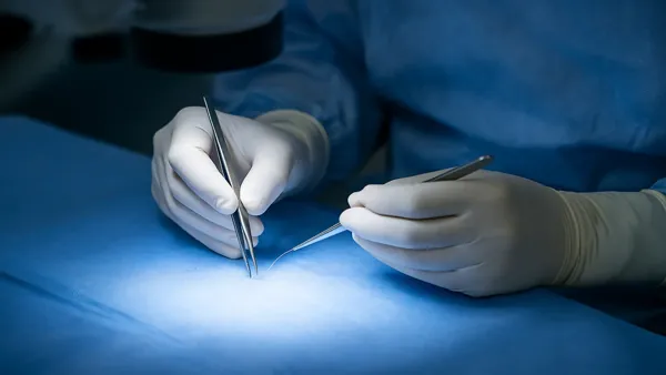 Mãos de cirurgião manipulando pinças microcirúrgicas durante reversão de vasectomia em Juiz de Fora